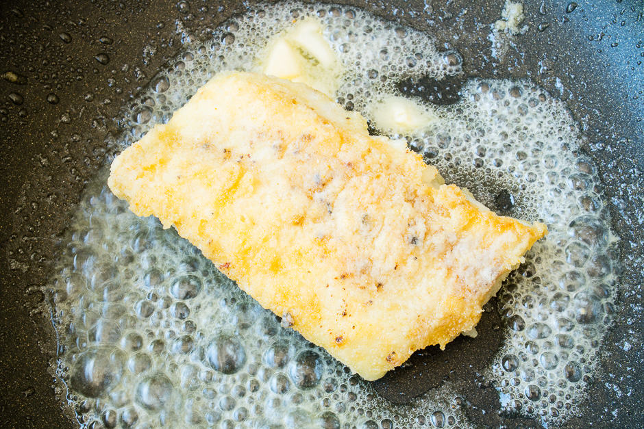 Fish fillet in the pan with foamed butter.
