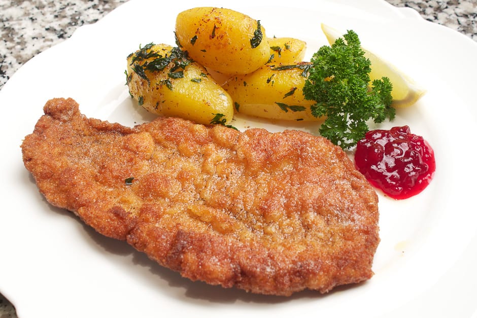 Wiener schnitzel served on a plate with cranberries and parsley potatoes.