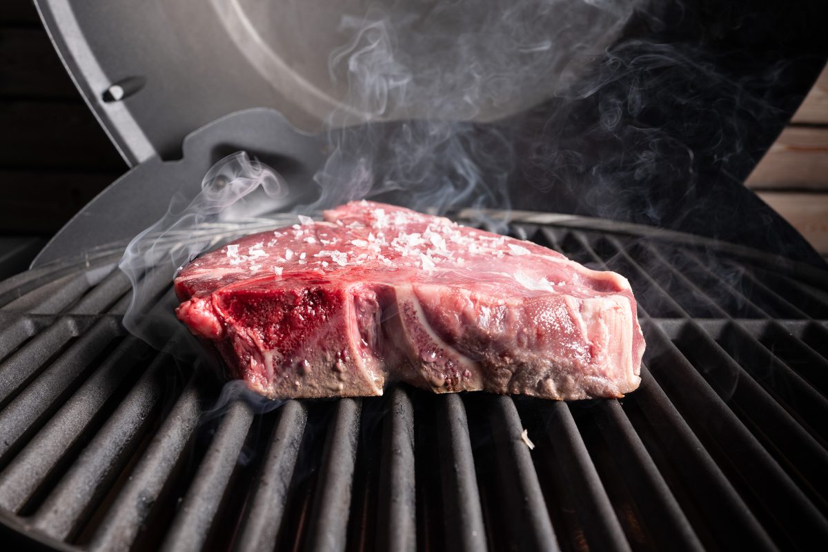 Porterhouse steak on the grill, photographed from the side with smoke.
